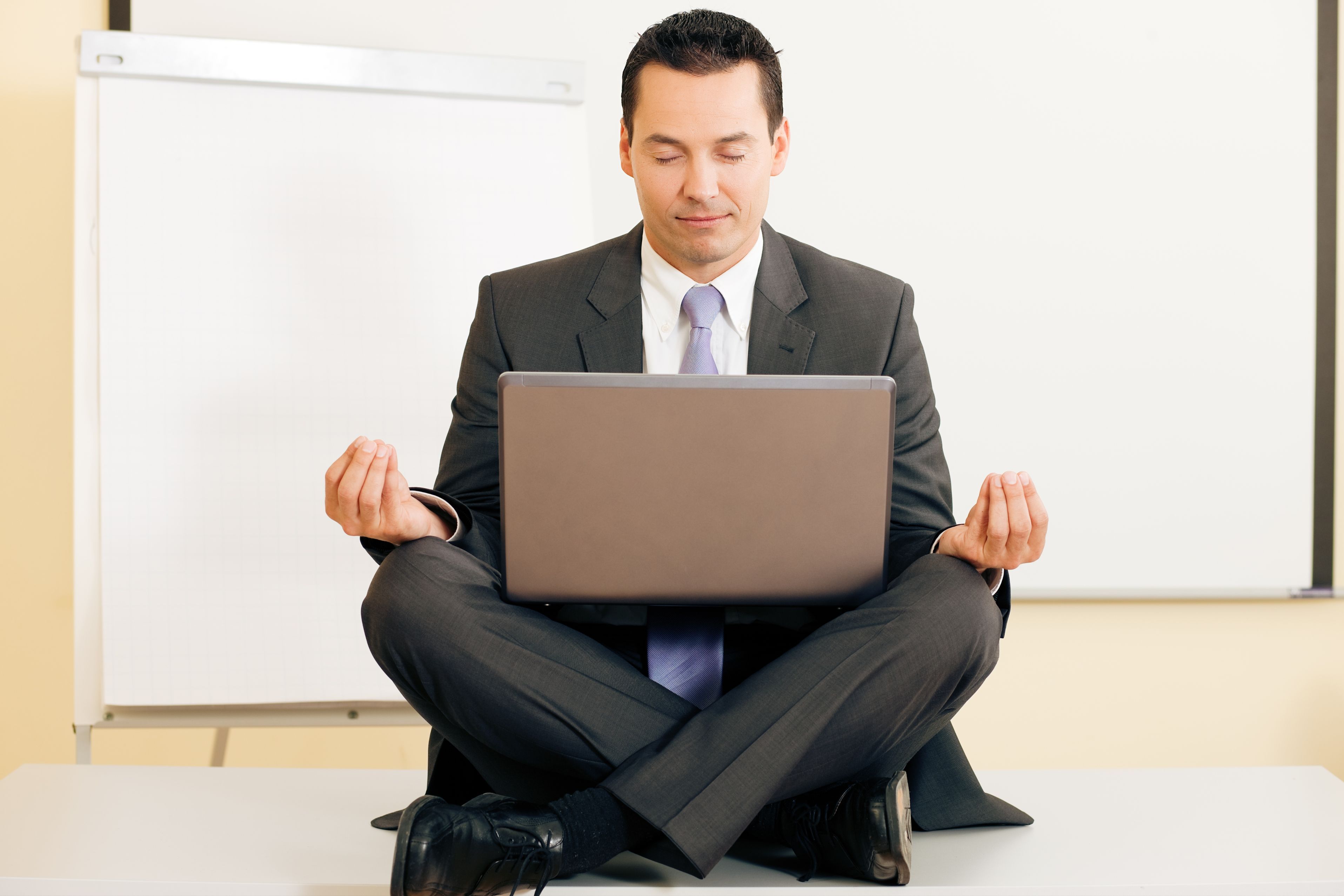 angajat in sezut, care face yoga cu un laptop pe picioare