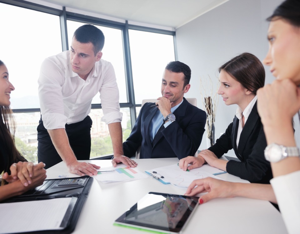 Mai mulți colegi de serviciu stau la o masă și discută.