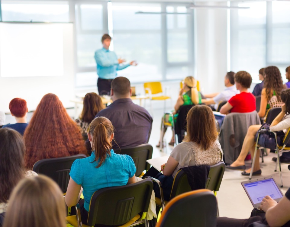 Un specialist de top în training le vorbește oamenilor din companii aflați într-o sală de curs