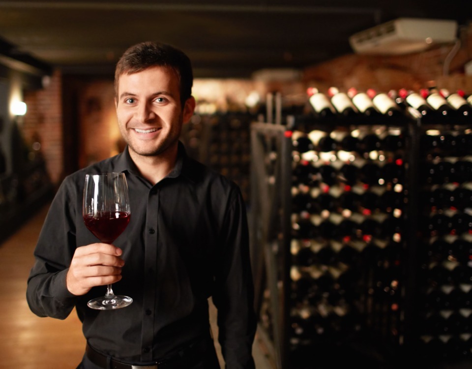 Bărbat cu un pahar de vin în mână, aflat într-o pivniță