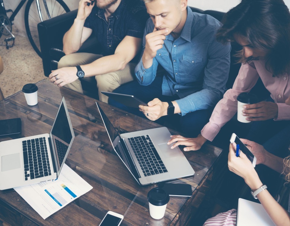 Spațiu de lucru la comun. Mai mulți tineri care lucrează pe laptopuri și tablete la un proiect comun.